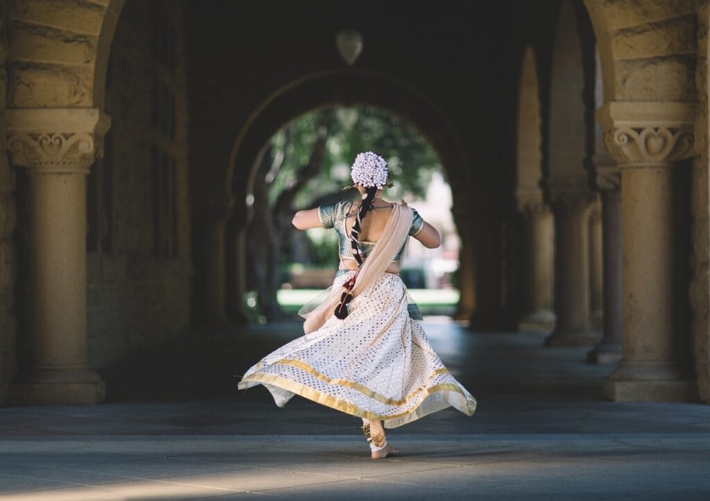 Woman in traditional Indian attire dancing under an arched hallway.